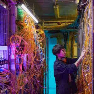 Wide angle side view at young network technician connecting wires and cables in server room, copy space